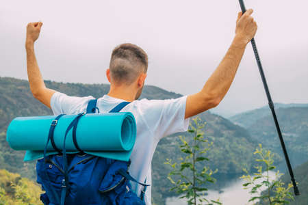 traveler or hiker in the mountains with backpack and arms up in the air