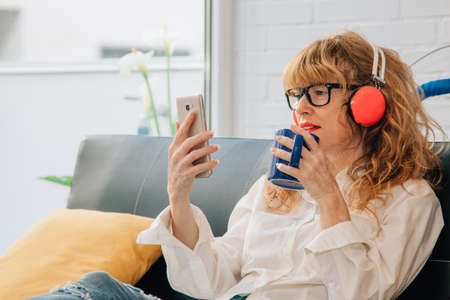 woman drinking coffee and listening to music with headphones and mobile phone at homeの写真素材