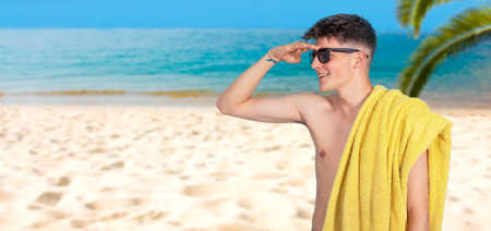 teen boy with towel and sunglasses on the beachの写真素材
