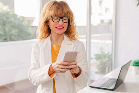 middle-aged blonde business woman with mobile phone in officeの写真素材