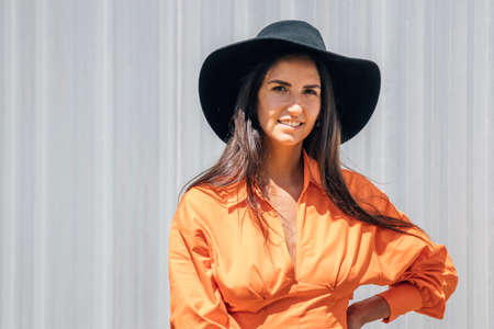 fashionable young girl in orange dress and hat on outdoor gray wall backgroundの写真素材