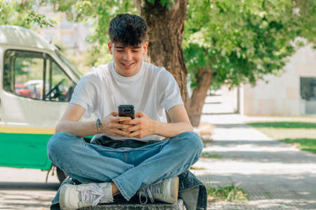 male teenager sitting on the street with mobile phone