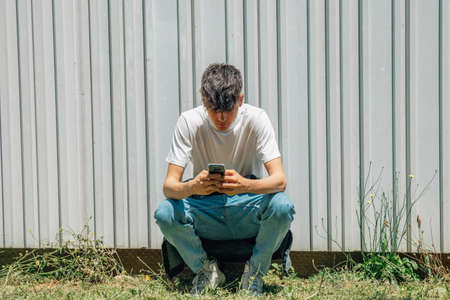 teen boy squatting with phone on the streetの写真素材