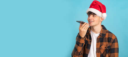 young man in santa claus hat sending voice message isolated on blue backgroundの写真素材