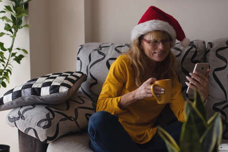woman at home with santa claus hat at christmas with mobile phoneの写真素材