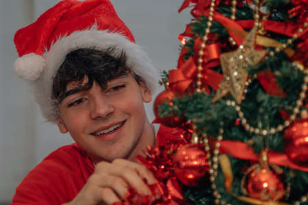 teenage boy decorating christmas tree at home with santa claus hatの写真素材