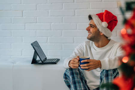 man in santa claus hat at home for christmas with laptopの写真素材
