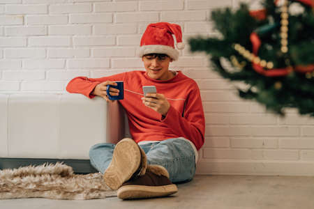 teenage boy with mobile phone and santa claus hat at home for christmasの写真素材