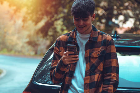 young man outdoor mobile phone leaning on the carの写真素材