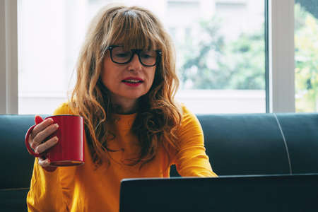 middle-aged adult woman at home with computer and cup of coffee