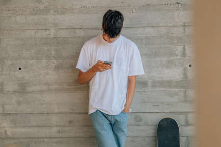 teenage boy with mobile phone and skateboard on the wall