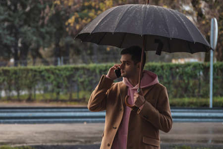 man on the street with umbrella and mobile phoneの写真素材
