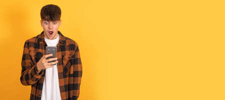 isolated teenager boy surprised looking at mobile phoneの写真素材