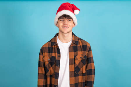 young man with santa claus hat isolated on blue colored backgroundの写真素材