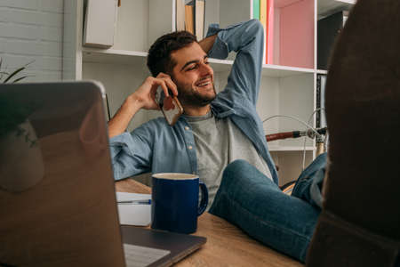 man at home relaxed with computer talking on mobile phoneの写真素材