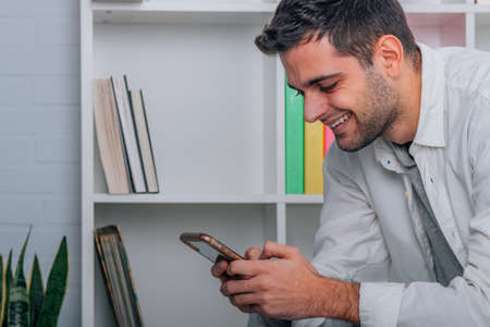 young man at home sitting on sofa looking at mobile phone