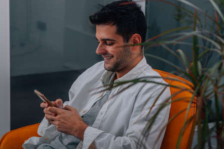 young man at home sitting on sofa looking at mobile phone