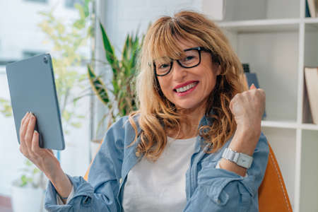 woman with success gesture looking at the computer or tablet at home