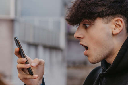 surprise or astonished teenager looking at mobile phone in the street