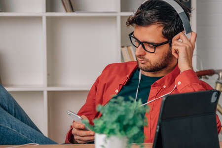 young man at home with mobile phone and headphones listening to musicの写真素材