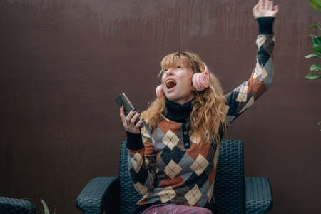 middle aged woman singing at home with mobile phone and headphones