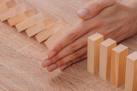 hand stops falling dominoes or wooden puzzle