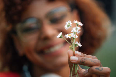 close-up of hand with flowers and portrait of girl smiling in background
