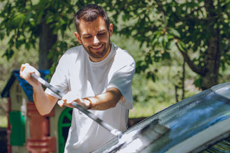 young man washing car in summer outdoorsの写真素材