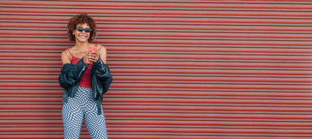urban style girl in summer on the street with mobile phone and red wall backgroundの写真素材