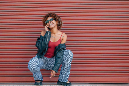 urban style girl in summer on the street with mobile phone and red wall backgroundの写真素材