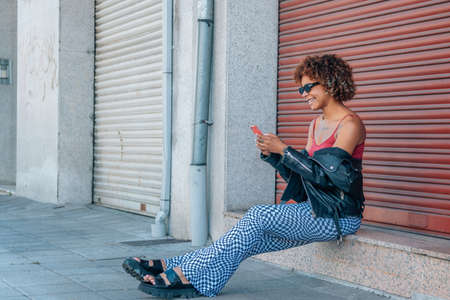 urban style black latin girl with mobile phone in the streetの写真素材