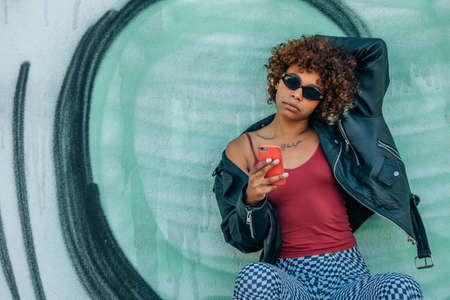 urban girl with mobile phone or smartphone on the wall in the streetの写真素材