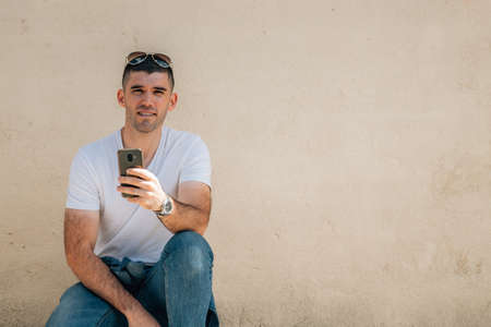 young man in the street with mobile phone with wall in background