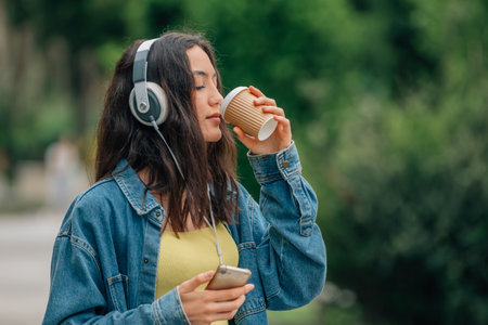 girl on the street with mobile phone and headphones and cup of coffee or soft drinkの写真素材