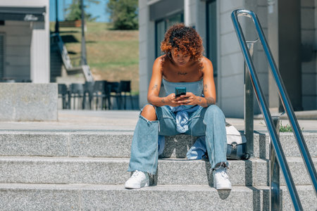 latin african american girl with mobile phone on stairs in city streetの写真素材