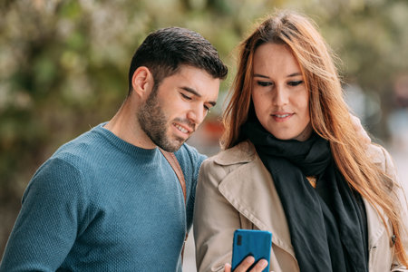 couple in autumn looking at mobile phone in the street outdoors