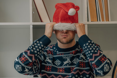 young man or teenager in christmas at home angry with santa claus hatの写真素材