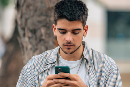 young millennial student looking at mobile phone on the streetの写真素材