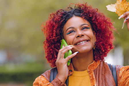 smiling black latin girl with red hair talking on mobile phone in autumn outdoors