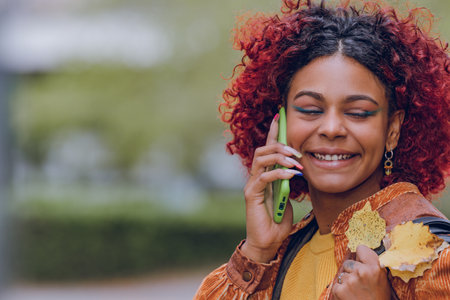 black latin american with mobile phone and autumn leaves outdoorsの写真素材