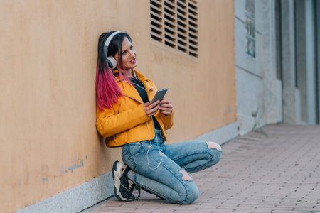 urban girl on the street sitting listening to music with headphones and mobile phoneの写真素材