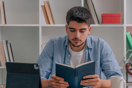 student at home studying or reading book with laptop on desk