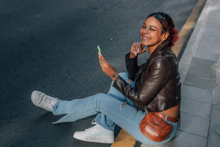 urban woman or girl with mobile phone sitting on street sidewalkの写真素材