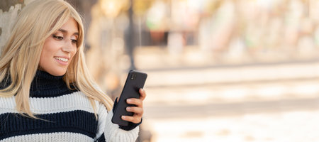 woman with autumn or winter sweater outdoors looking at mobile phone or cellの写真素材