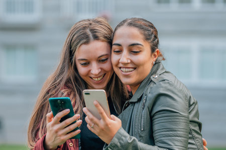 friends with mobile phones smiling hugging in the streetの写真素材