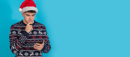 isolated young man in christmas clothes and santa claus hat with mobile phone or smartphoneの写真素材