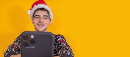 isolated young man in christmas clothes and santa claus hat with mobile phone or smartphone