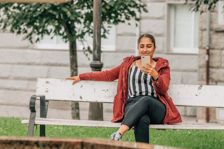 young woman or girl with mobile phone on park benchの写真素材