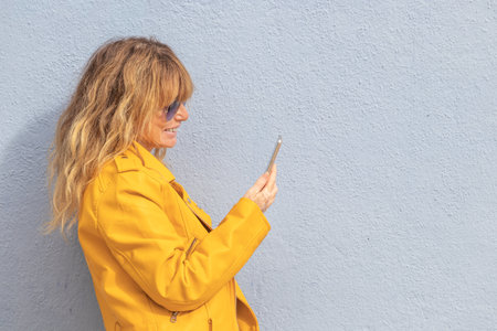 middle age woman with mobile phone isolated on street wall with copy-spaceの写真素材