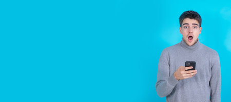 surprised young man with mobile phone or smartphone isolated on blue backgroundの写真素材